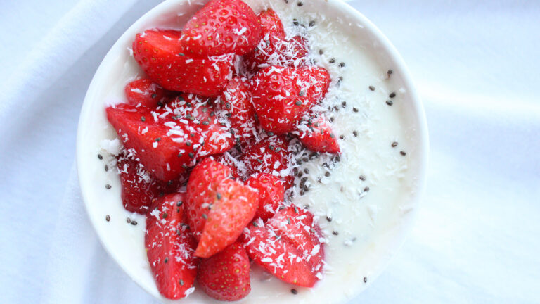 A bowl of white coconut yogurt with strawberries and chia seeds